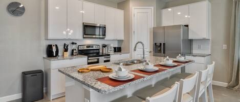 A modern kitchen with white cabinets, a granite countertop, and a central island with chairs.