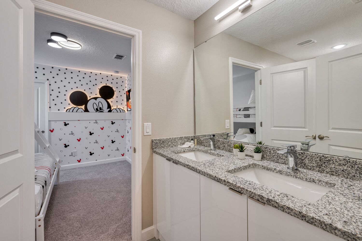 Une salle de bain moderne avec un double lavabo, un grand miroir et un mur décoré sur le thème de Mickey Mouse.