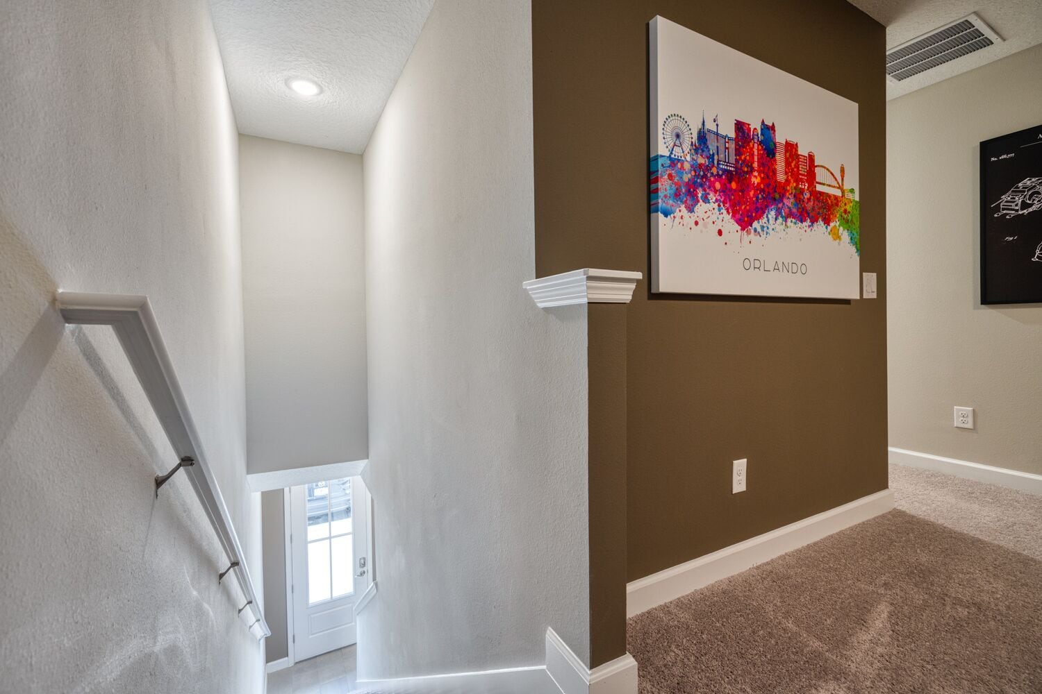 A hallway with a framed cityscape artwork labeled 'ORLANDO' on the wall, carpeted flooring, and a white door at the end.