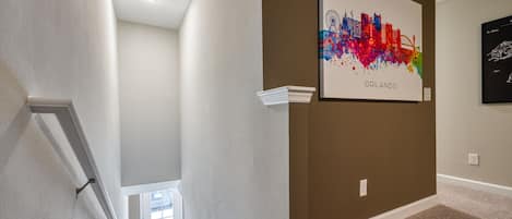 A hallway with a framed cityscape artwork labeled 'ORLANDO' on the wall, carpeted flooring, and a white door at the end.