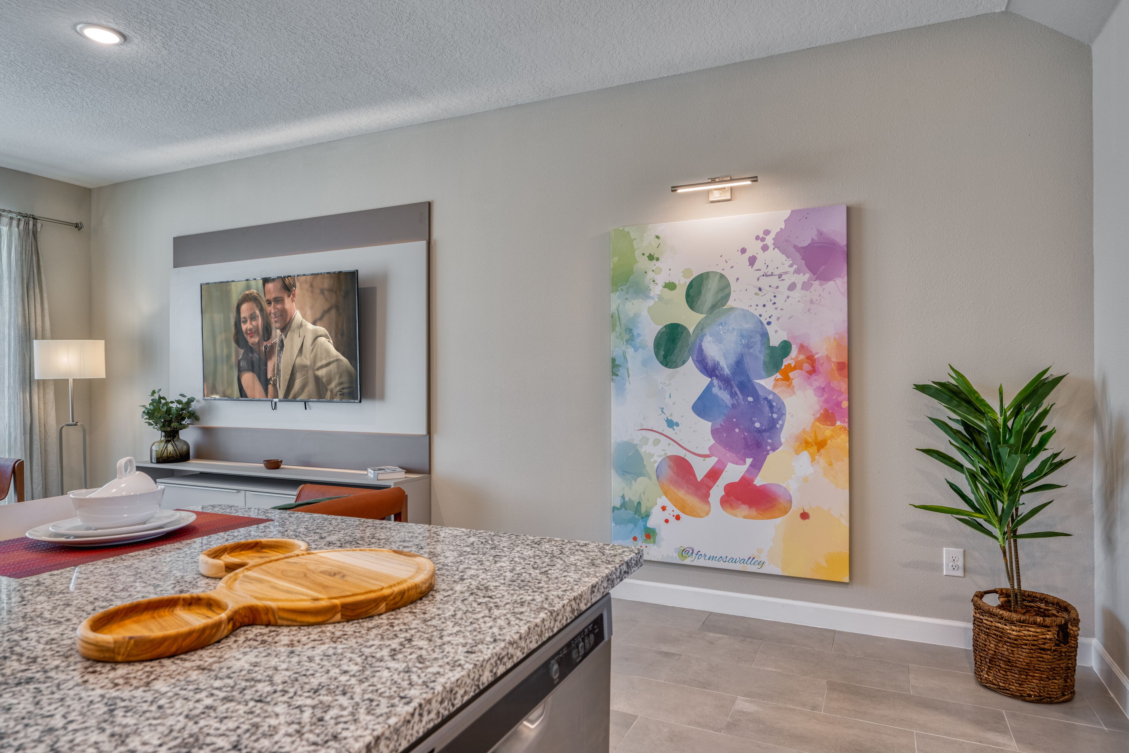 A modern kitchen with granite countertops, a dishwasher, and a dining area with a table set for two.