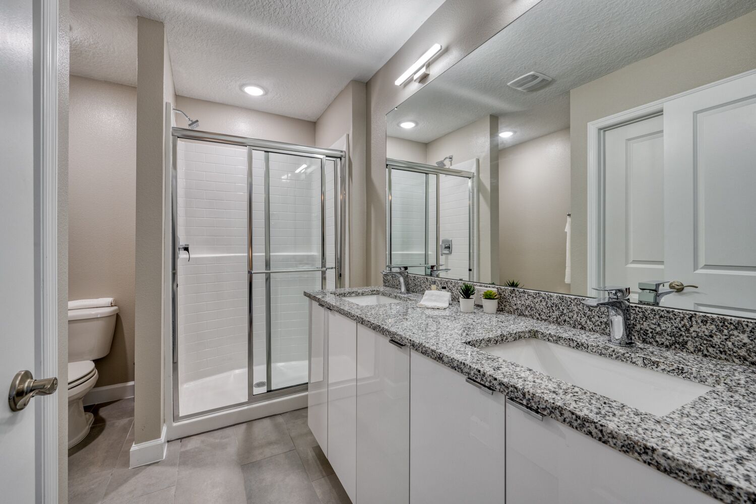 Un baño moderno con cabina de ducha, un tocador grande con encimera de granito y un espejo de cuerpo entero.