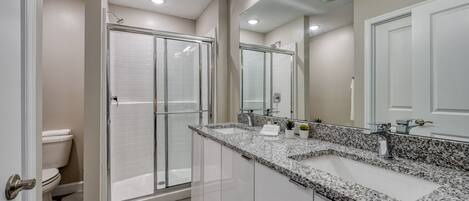 Un baño moderno con cabina de ducha, un tocador grande con encimera de granito y un espejo de cuerpo entero.