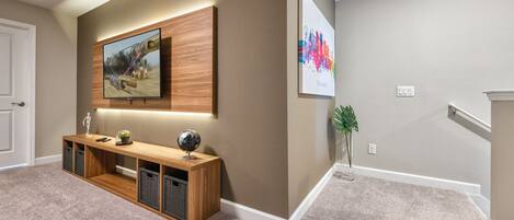 A hallway with a wooden console table, a mounted TV, and a framed picture on the wall.