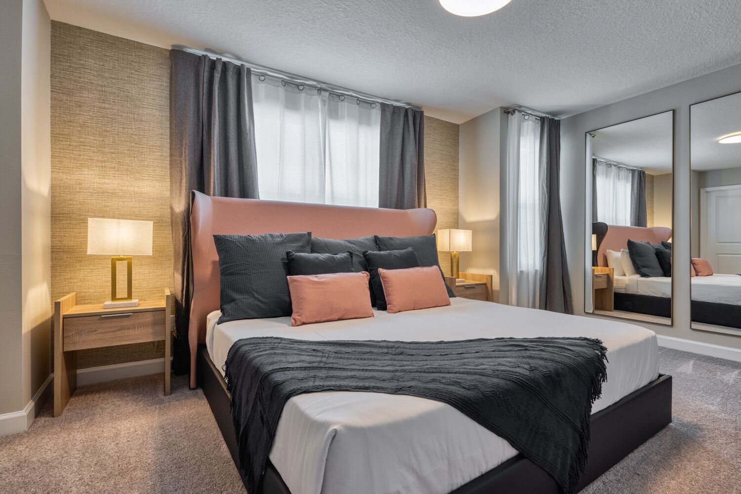 Ein modernes Hotelzimmer mit einem großen Bett, zwei Nachttischen mit Lampen, einem großen Spiegel und einem Teppichboden.