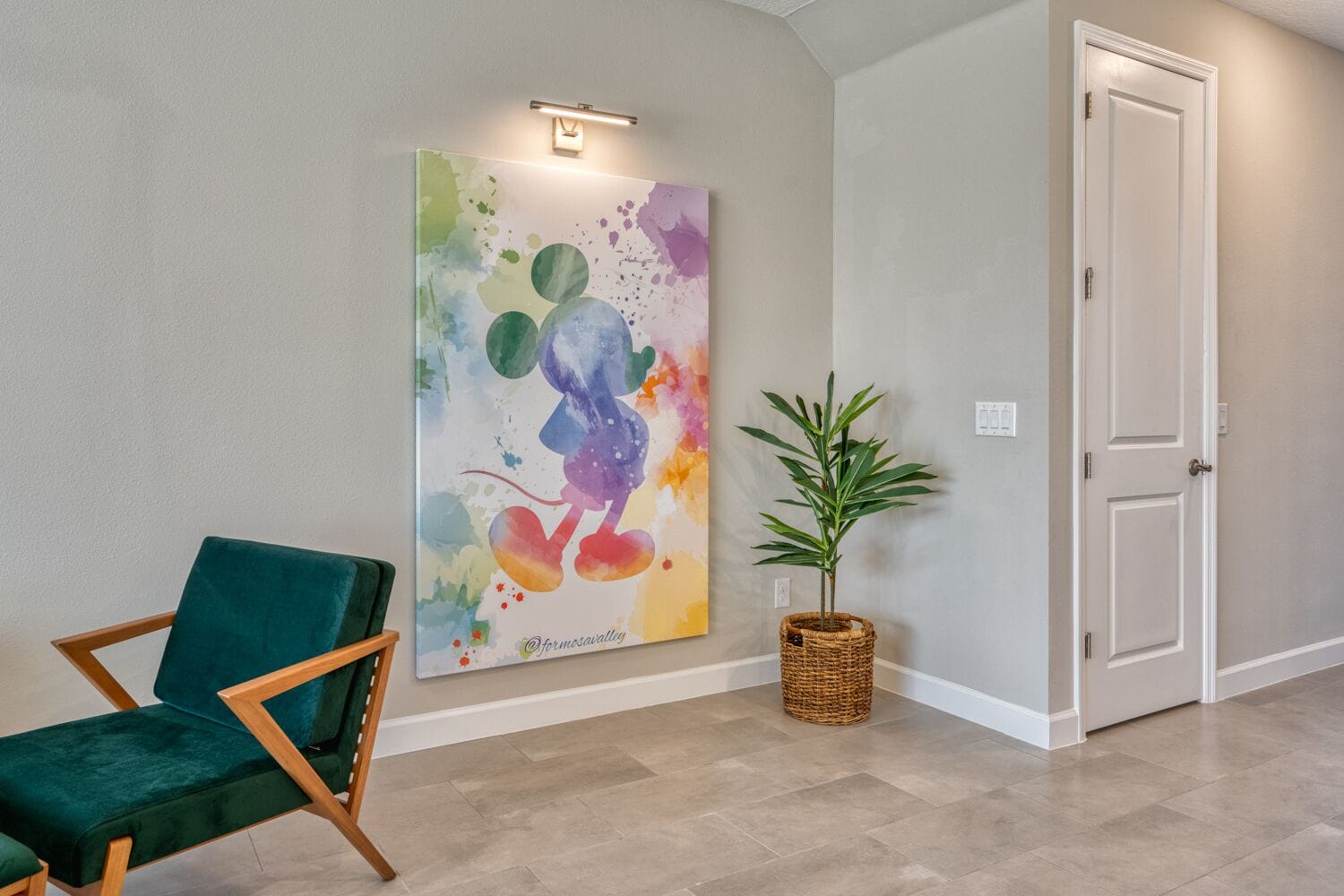 A hallway with a green chair, a wall-mounted abstract painting, a potted plant, and a door.