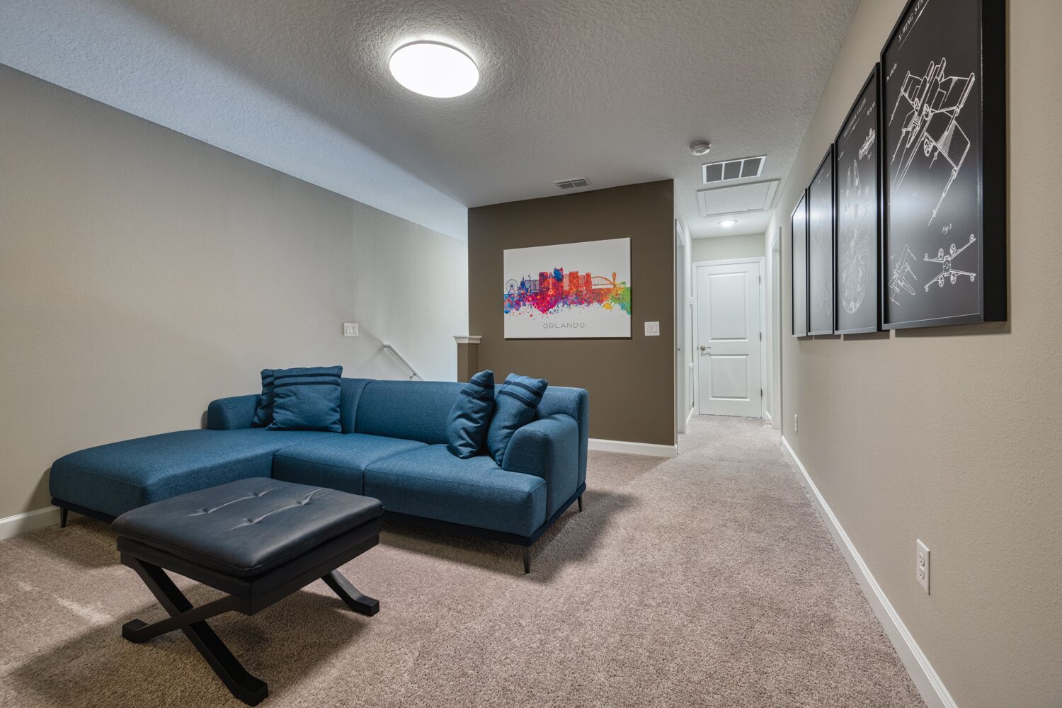 A home interior with a sectional sofa, a bench, a colorful artwork on the wall, and framed pictures.