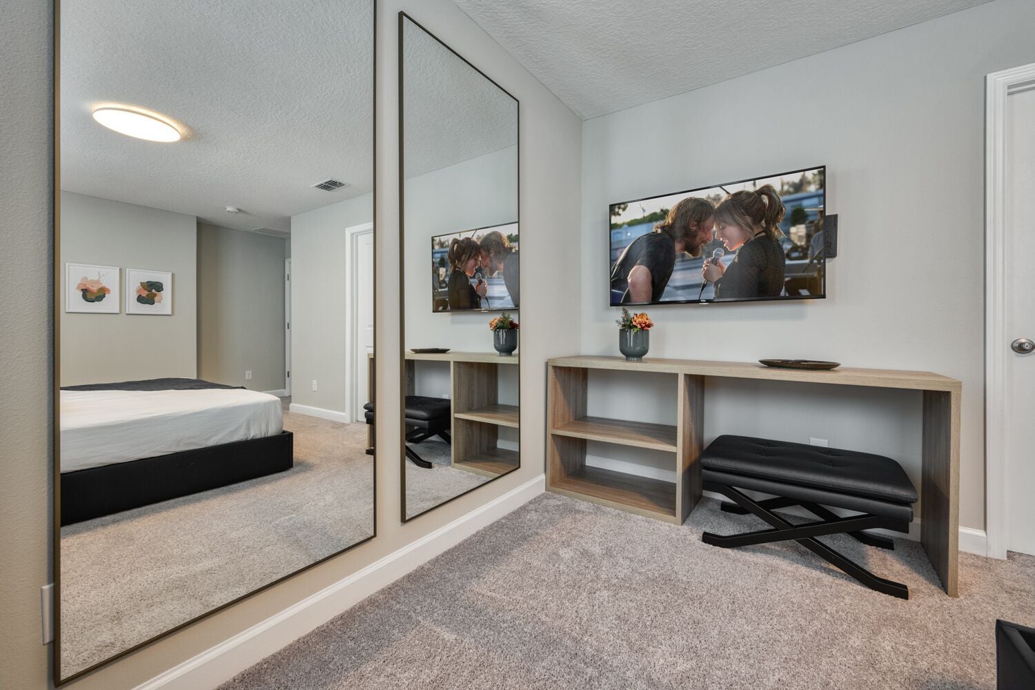 A modern bedroom with a bed, a desk, a chair, a TV, and a large mirror.