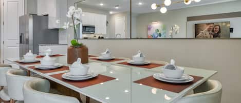 A modern dining area with a long table set for six, surrounded by cushioned chairs.