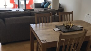 A living room with a wooden dining table, a grey sofa, and orange chairs. - Penthouse apartment with stunning sea view Westward Ho! (Westward Ho!)