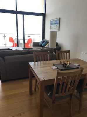 A living room with a wooden dining table, a grey sofa, and orange chairs.
