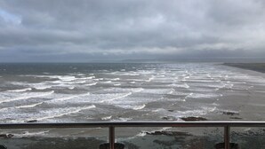 A coastal view with waves crashing onto the shore, a cloudy sky, and a metal railing in the foreground. - Penthouse apartment with stunning sea view Westward Ho! (Westward Ho!)