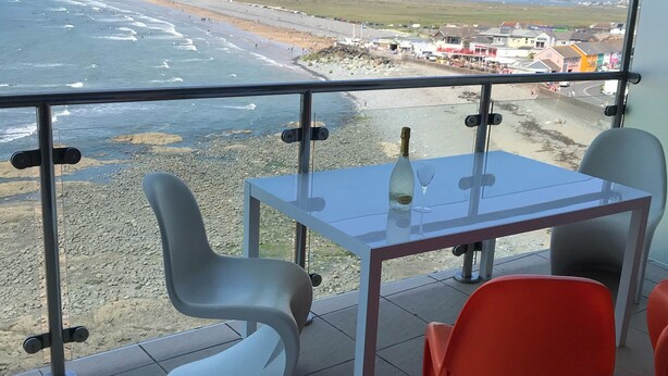 A balcony with a table and chairs, overlooking a beach and town. - Penthouse apartment with stunning sea view Westward Ho! (Westward Ho!)