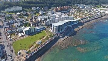 Vue aérienne d’une ville côtière avec des bâtiments modernes, une promenade et des eaux cristallines.