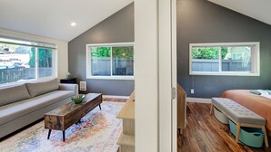 Un salon moderne avec un canapé, une table basse en bois et un banc. Il y a deux fenêtres donnant sur un jardin.