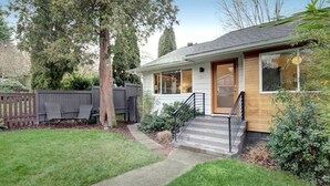Une maison de plain-pied avec un porche à l’avant, une porte en bois et un petit jardin devant, avec un chemin menant à la porte.