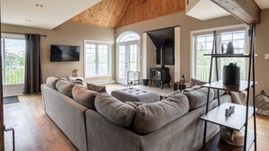 A spacious living room with a large grey sectional sofa, a black wood-burning stove, and a wooden ceiling.