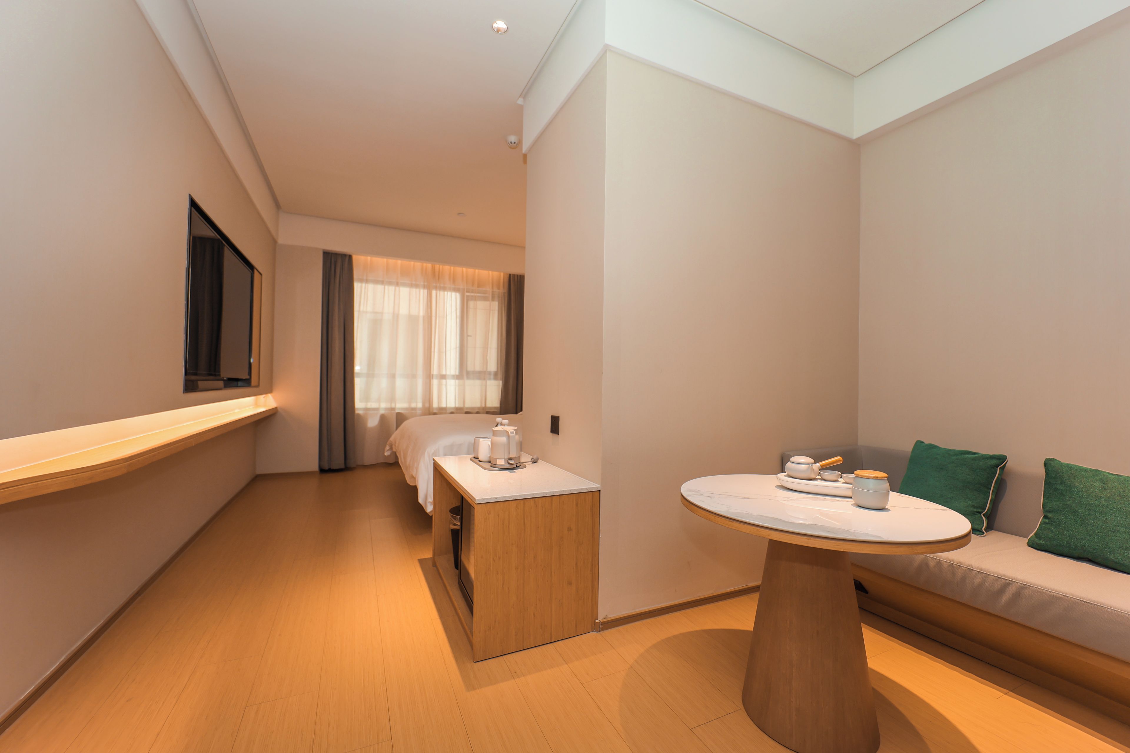 A modern hotel room with a bed, a small table, a sofa, and a window with curtains.
