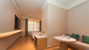 A modern hotel room with a bed, a small table, a sofa, and a window with curtains. - Ji Hotel (Nanjing)