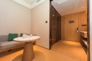 Una habitación de hotel moderna con un sofá, una mesa redonda, una puerta de madera y un área de baño.