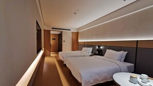 A hotel room with two beds, a bedside table with a lamp, and a view of the hallway.