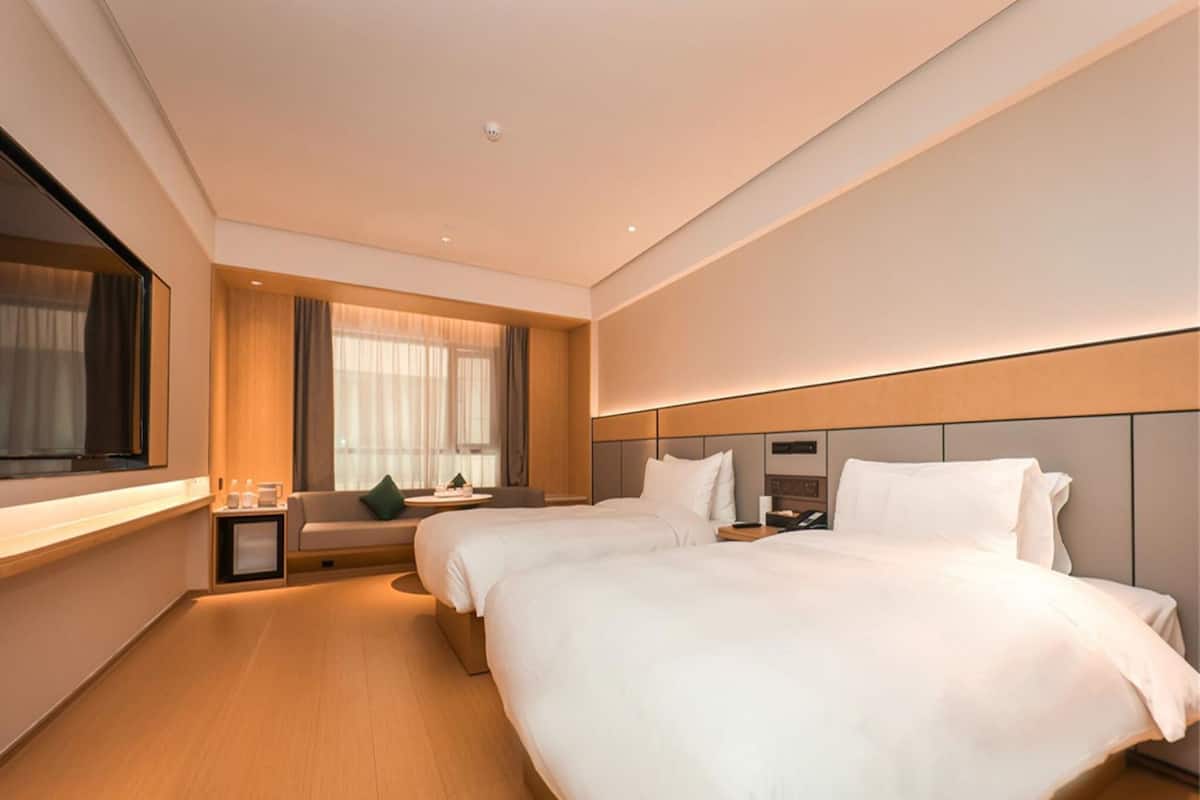 A modern hotel room with two beds, a sofa, a small table, and a TV.