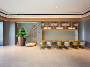 A modern interior with a large potted tree, a bookshelf, and a dining area with wooden tables and chairs. - Ji Hotel (Nanjing)