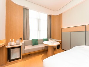 A hotel room with a bed, a sofa, a small table with a tray of tea, a minibar, and a large window with curtains. - Ji Hotel (Nanjing)