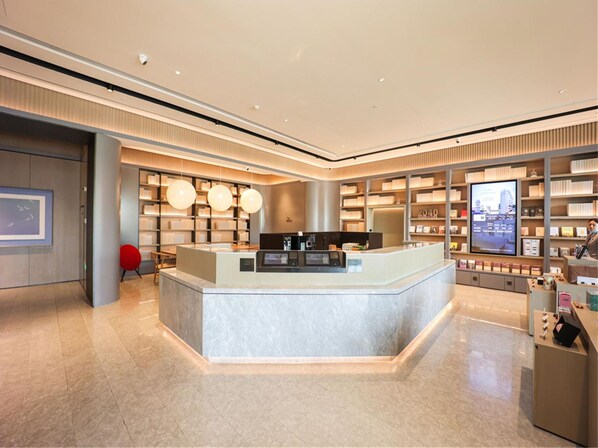 A modern hotel lobby with a reception desk, seating area, and book-lined shelves.