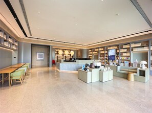 A modern hotel lobby with a reception desk, seating area, and bookshelves. - Ji Hotel (Nanjing)