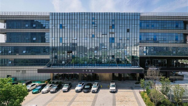 A modern hotel with a glass facade, a covered entrance, and a parking lot with several cars. - Ji Hotel (Nanjing)