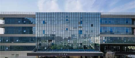 A modern hotel with a glass facade, a covered entrance, and a parking lot with several cars.