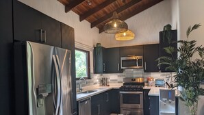 Una cocina moderna con armarios oscuros, electrodomésticos de acero inoxidable, salpicadero azulejado y una lámpara colgante.
