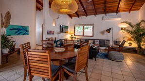 Un salón amplio con techo de madera, una mesa de comedor con sillas, un sofá y un televisor.