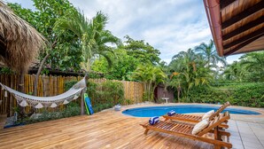 Una terraza de madera con piscina, sillas de descanso y una hamaca.
