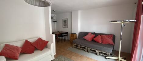 A living room with a white sofa, red cushions, a grey sofa with red cushions, a dining table with chairs, and a floor lamp.