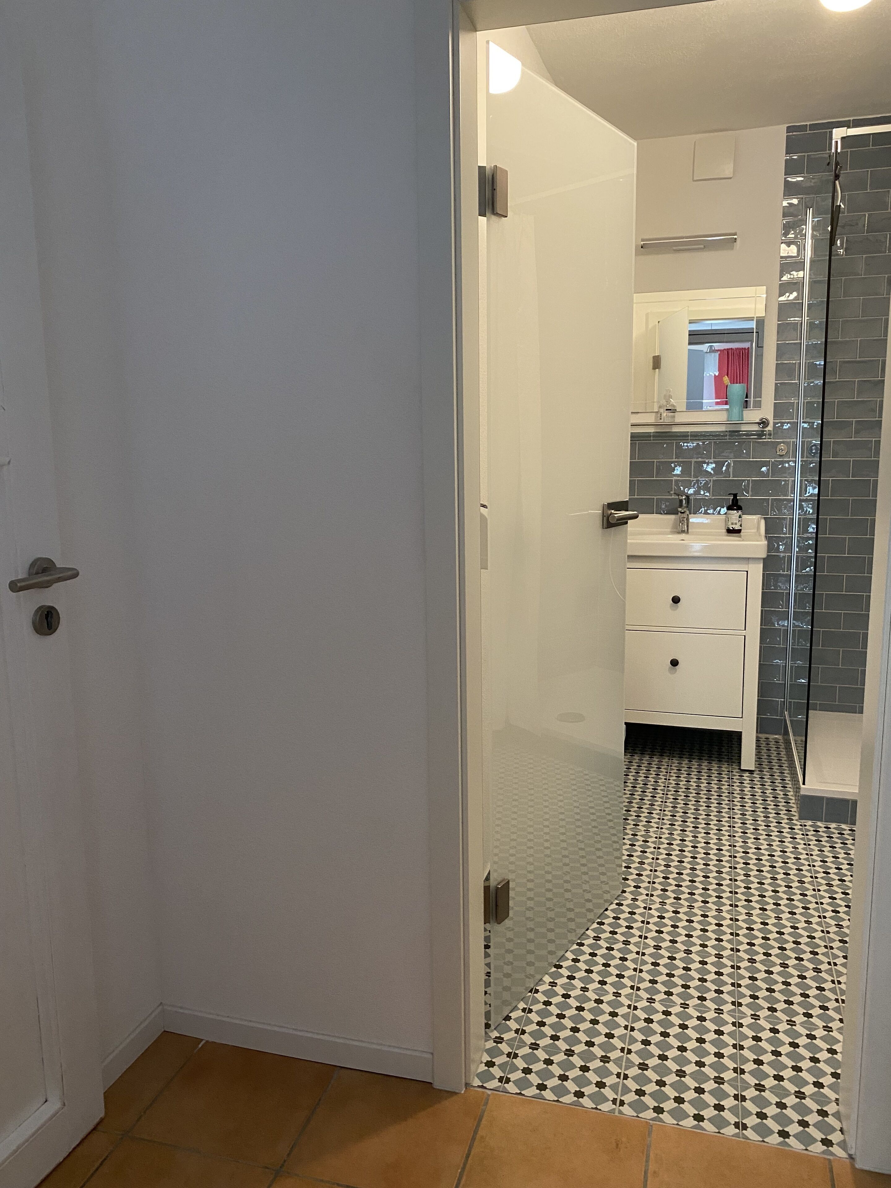Een badkamer met betegelde vloer, een wastafel en een glazen douchecabine.