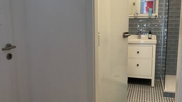 Een badkamer met betegelde vloer, een wastafel en een glazen douchecabine.