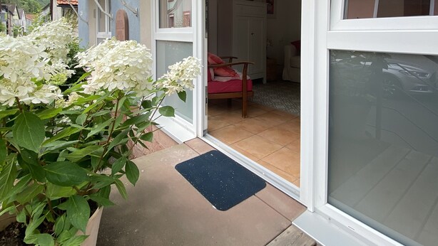 A house with a sliding glass door leading to a room with a pink chair and a wooden table. - Beautiful studio for 2 people in picturesque Homburg am Main (Triefenstein)