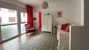 A modern living room with a sliding glass door, a red chair, a white sofa, a patterned rug, and a ceiling fan. - Beautiful studio for 2 people in picturesque Homburg am Main (Triefenstein)
