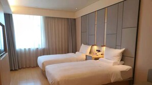 Habitación de hotel con dos camas, una mesita de noche, una lámpara, una ventana con cortinas y vistas al exterior.