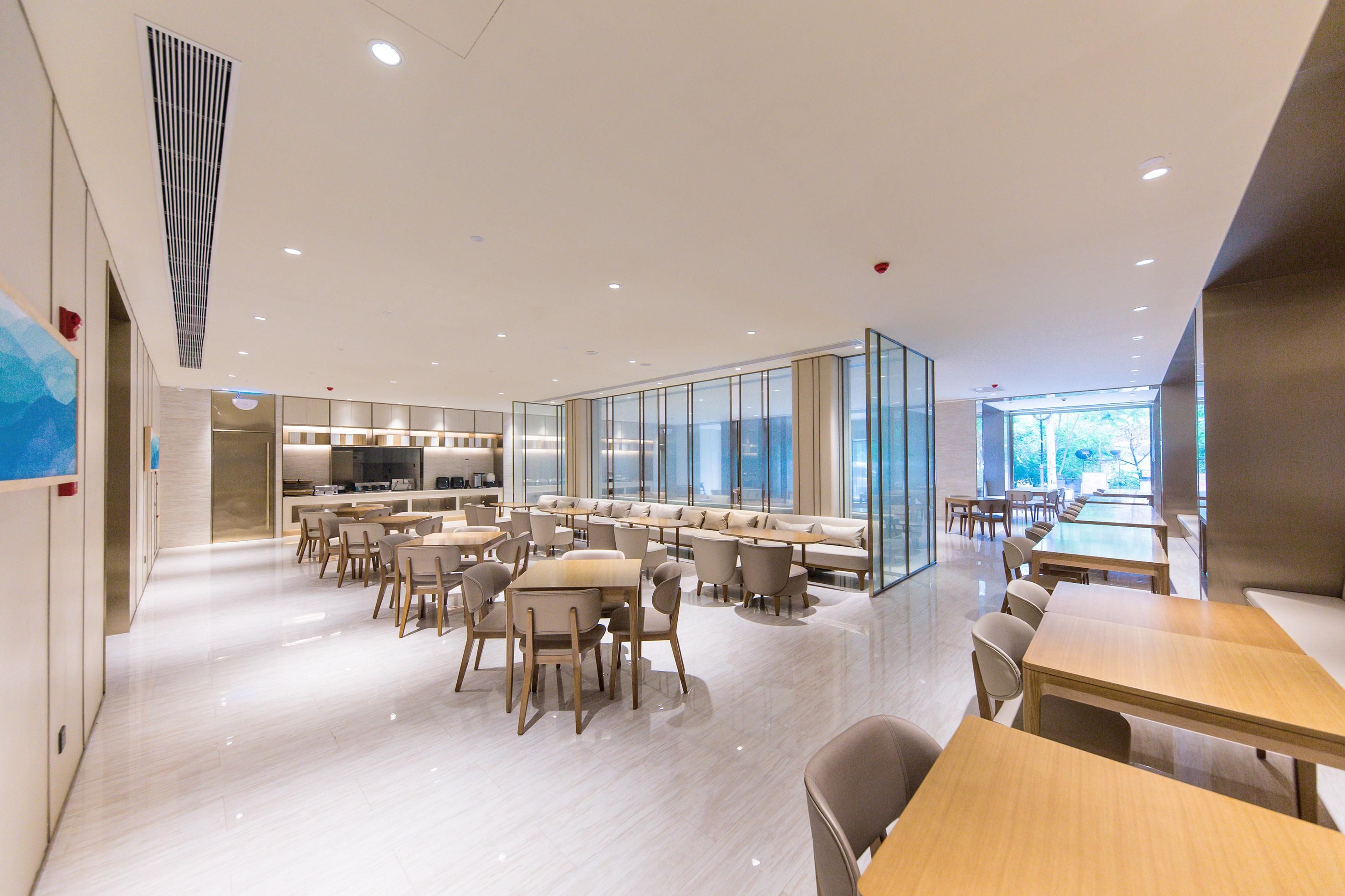 Un espace repas moderne doté de plusieurs tables et chaises, d’une cloison en verre et offrant une vue sur l’extérieur.