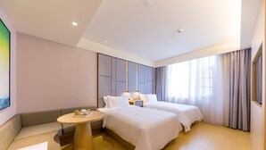 Habitación de hotel con dos camas, un sofá, una mesa redonda y un ventanal grande con cortinas.
