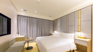 Una habitación de hotel moderna con una cama grande, mesitas de noche, una pequeña mesa redonda y un sofá.