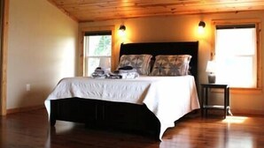 Un dormitorio con techo de madera, una cama con colcha blanca, dos almohadas y una mesita de noche con lámpara.