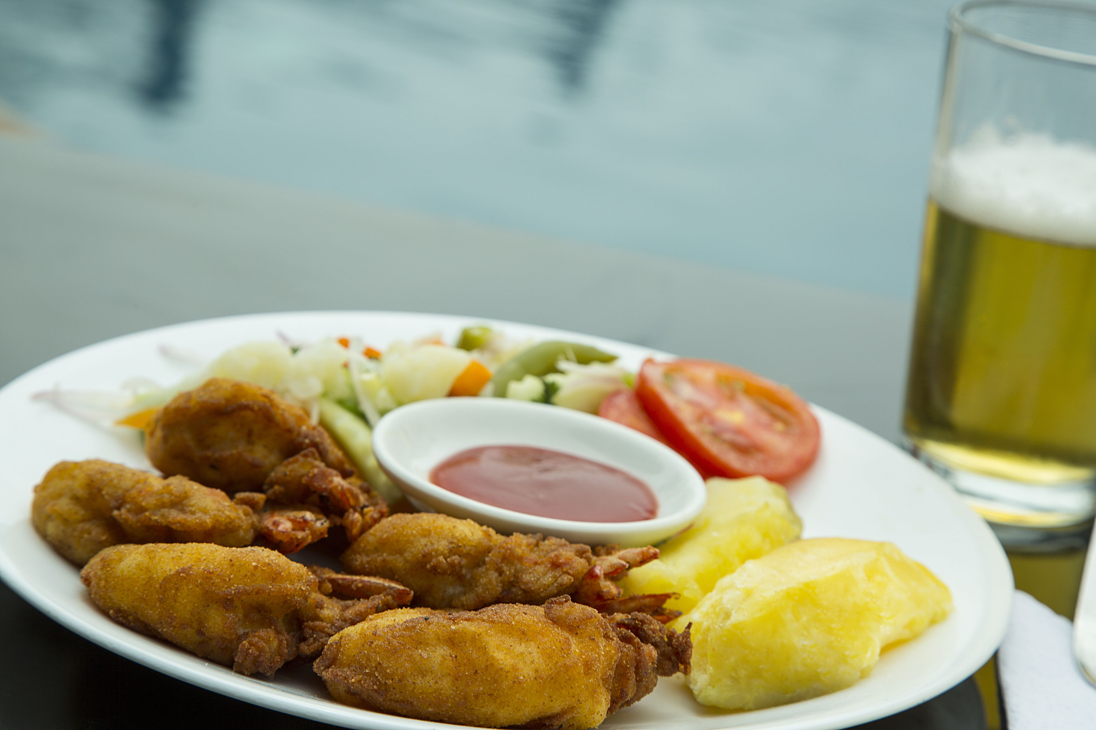 A plate of fried chicken, coleslaw, a slice of tomato, and a glass of beer.