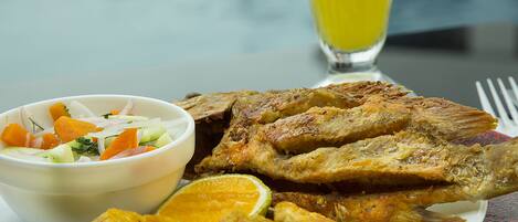 Un plato de pescado frito y plátanos fritos, acompañado de una ensalada y un vaso de jugo de naranja.