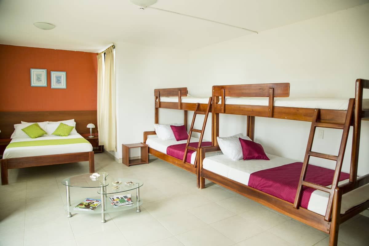 Quarto de hotel com uma cama beliche, uma cama de solteiro, uma mesa de centro de vidro e uma pequena mesa de cabeceira.