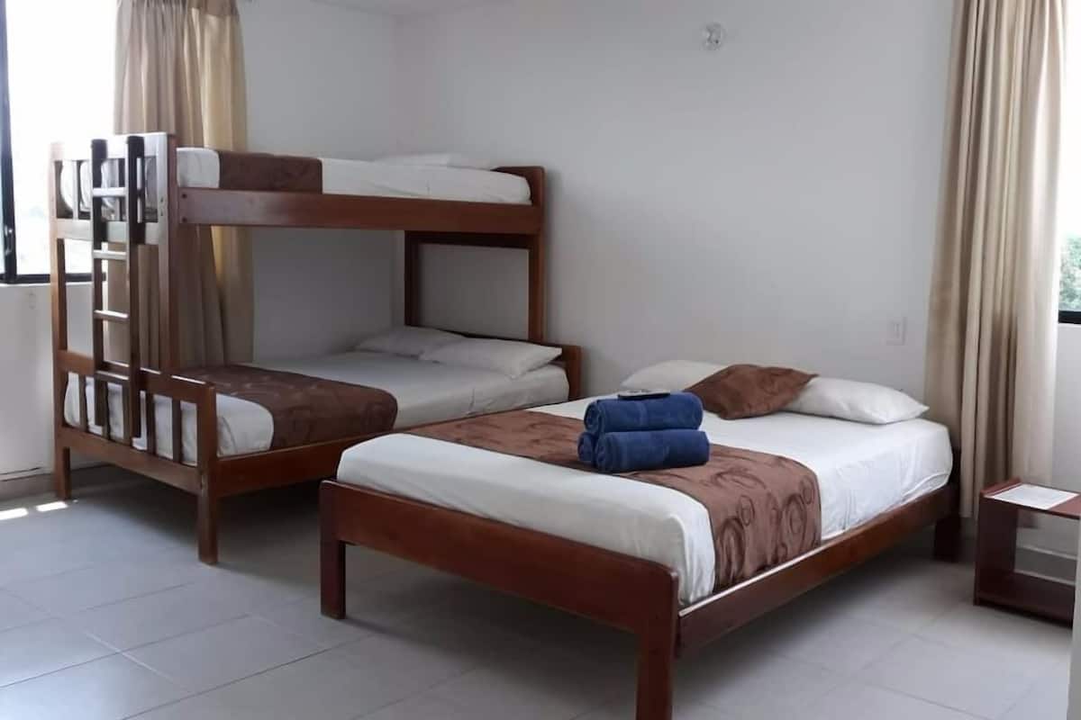 Um quarto com duas camas beliches de madeira, uma mesinha e uma janela com cortinas.