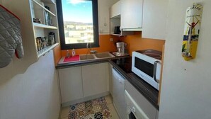 A compact kitchen with white cabinets, a microwave, a sink, and a window with a view of buildings.
